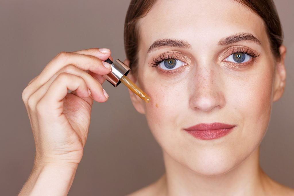 Portrait of young woman holding dropper with serum, skin care concept.